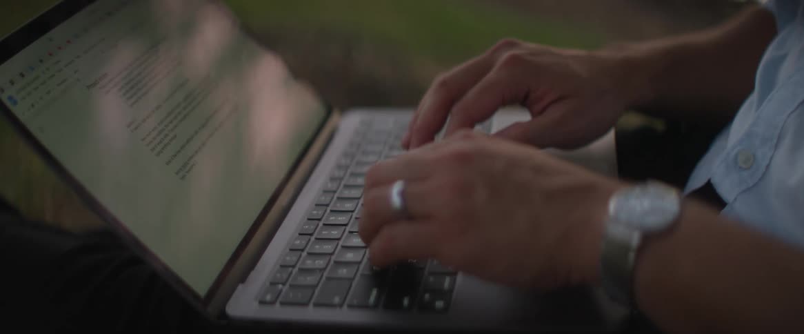 A man typing on a laptop while sitting on the ground at dusk