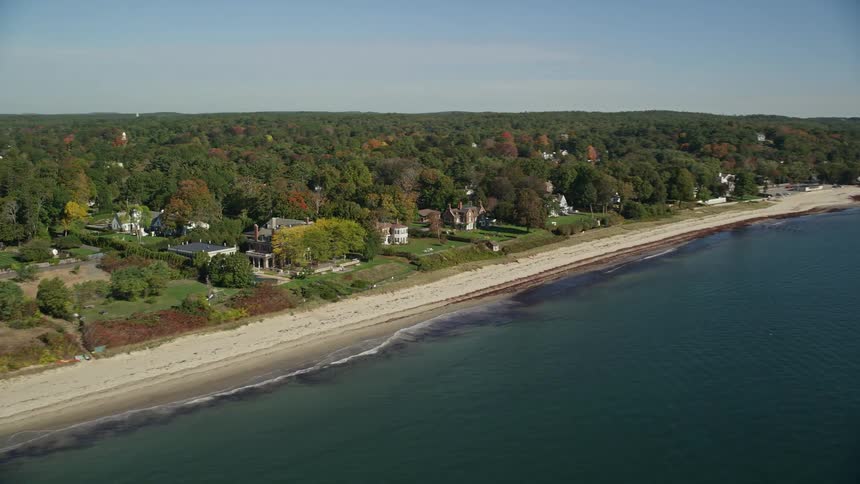 Aerial of large houses surrounded by autumn trees along an ocean shore