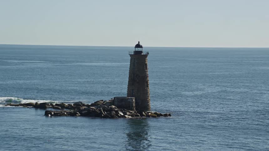 Waves splash against rocks around a lighthouse off the coast