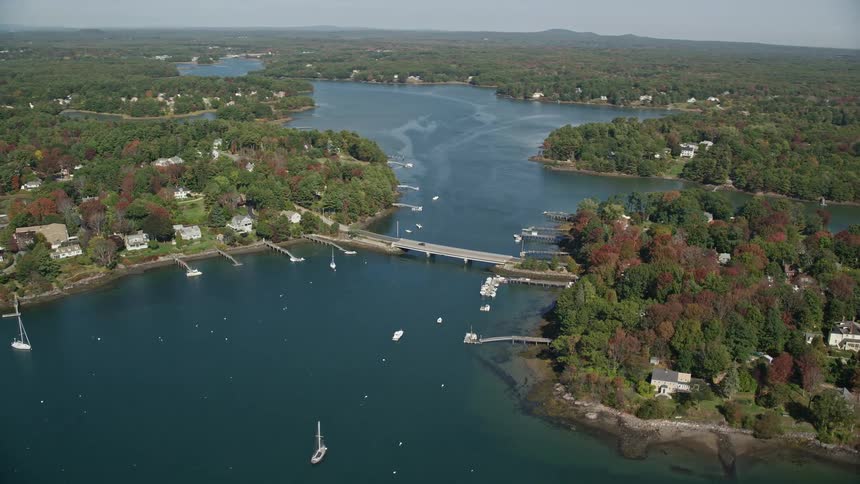 An aerial view of a waterfront land that faces a blue lake and a river with some boats above
