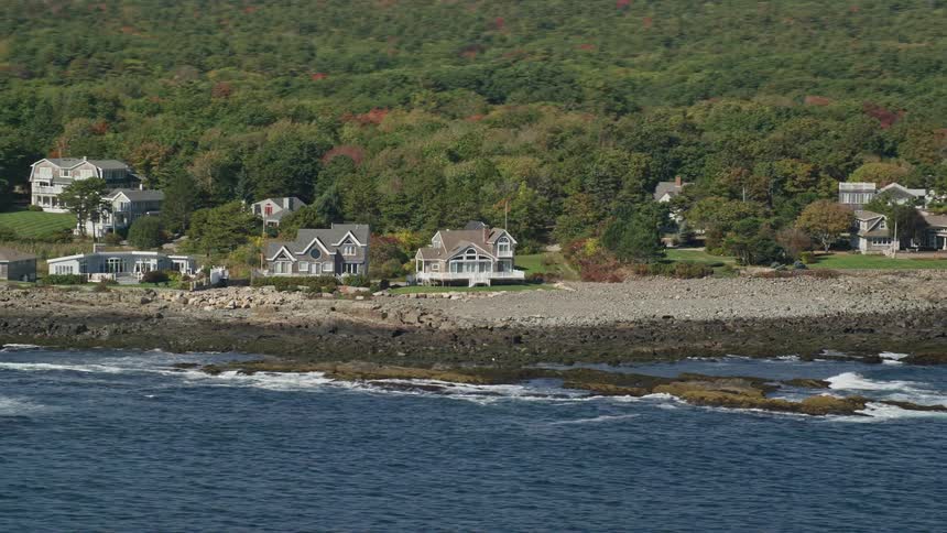 A residential area on top of rocks in front of the ocean coast and behind a dense forest