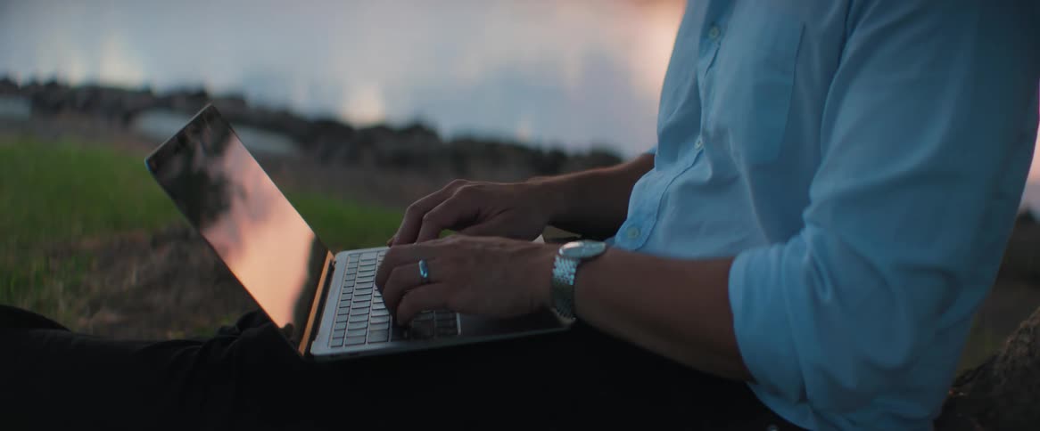 A man typing on a laptop sitting in nature