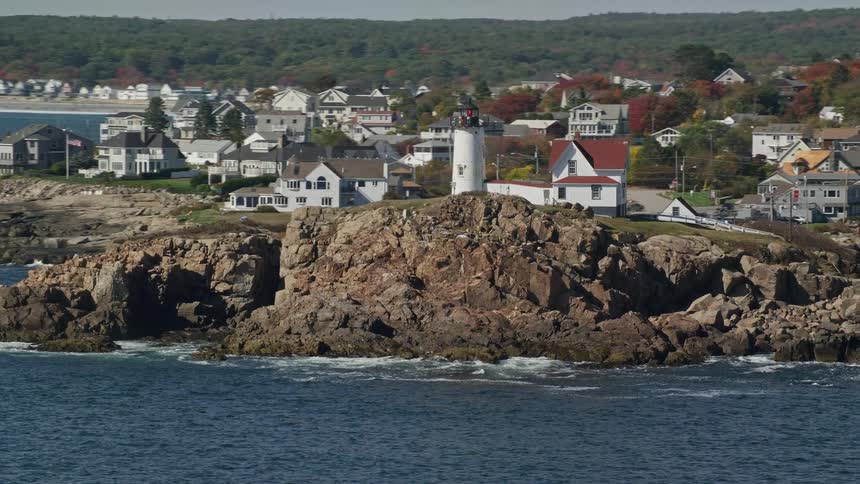 A white lighthouse on top of a rock facing the sea and behind a residential area