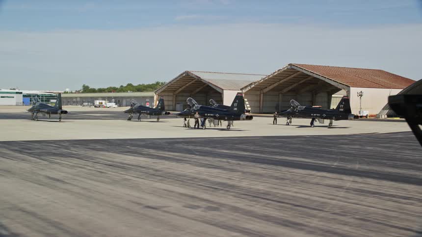 A drone flying over a hangar with some jets parked outside