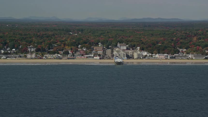 A beach facing the sea and with several small houses and a forest behind