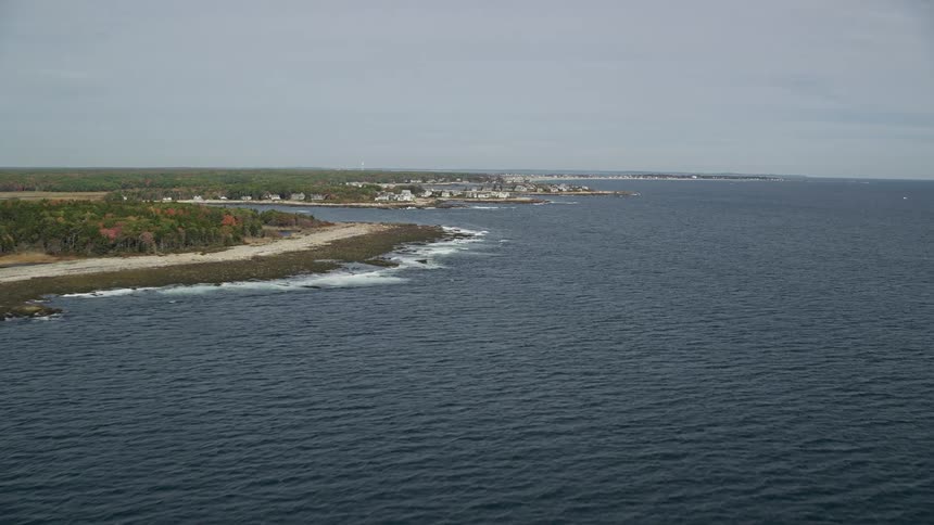 Aerial panorama of the sea by the edge of a peninsula surrounded by vegetation and residences on the horizon