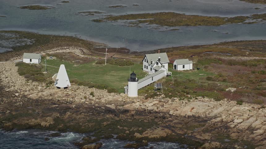 Aerial view of a small house next to a seaside lighthouse