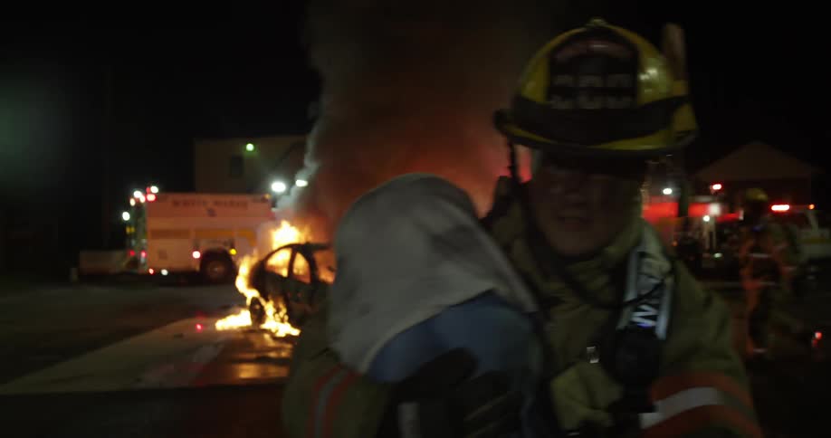 A fireman carries a boy away from burning cars