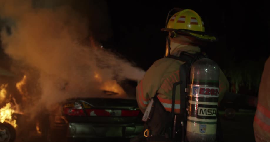 A firefighter is hosing a fire at night