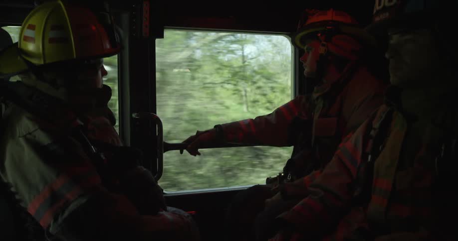 Firefighters riding in the back of a firetruck
