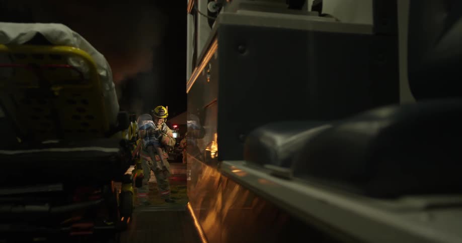 A firefighter lifting a boy near a moving vehicle at night