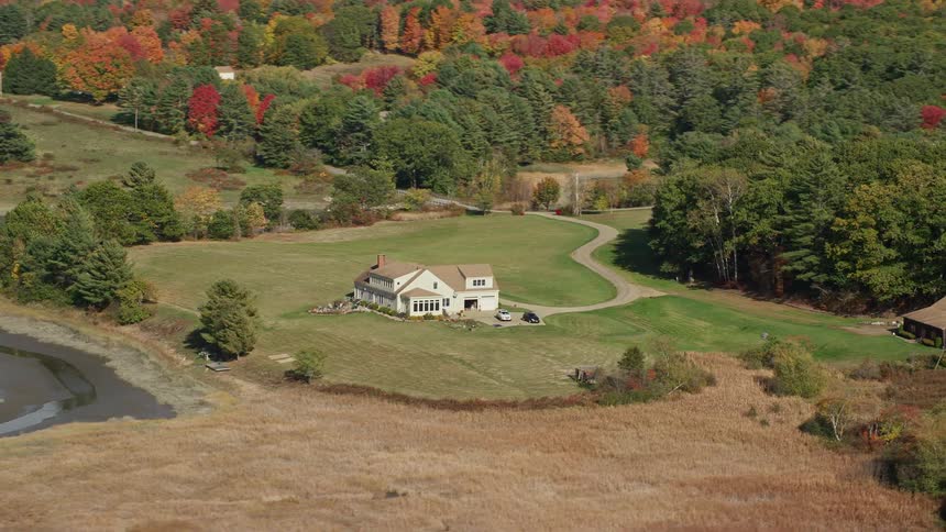 A stream runs near a house in a rural neighborhood surrounded by woods with trees in fall colors