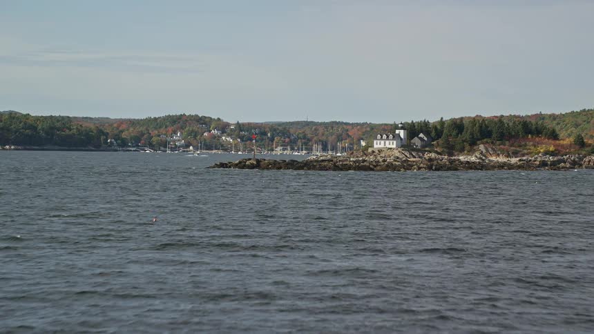 A sea coast full of rocks and behind a residential area with lots of trees