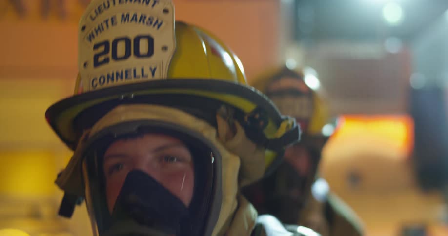 Fireman walk outside with bright lights shining behind