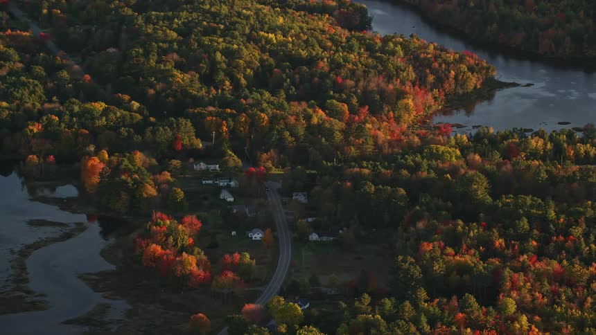 Aerial panorama of houses by the edge of a highway surrounded by forests and a lake