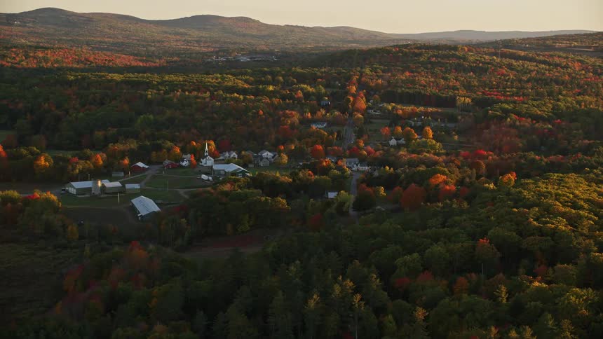 Aerial view of a river and a small town surrounded by red and brown trees at sunset