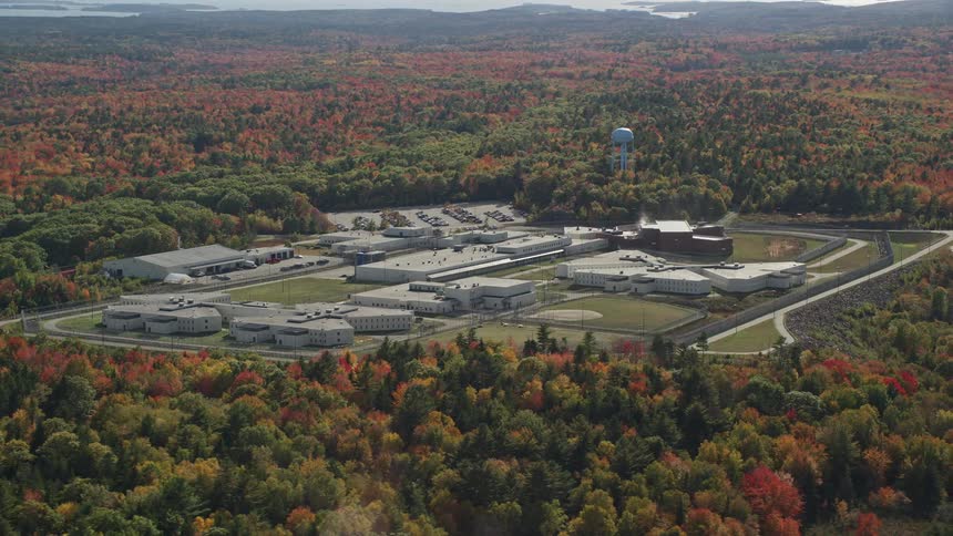 Woods surround manufacturing complex with a body of water in the distance