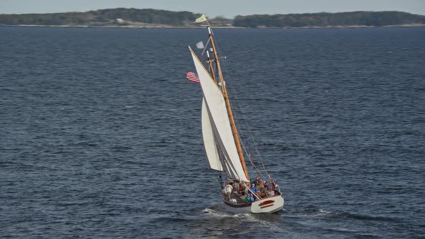 A sailboat filled with people moves across the water off the coast