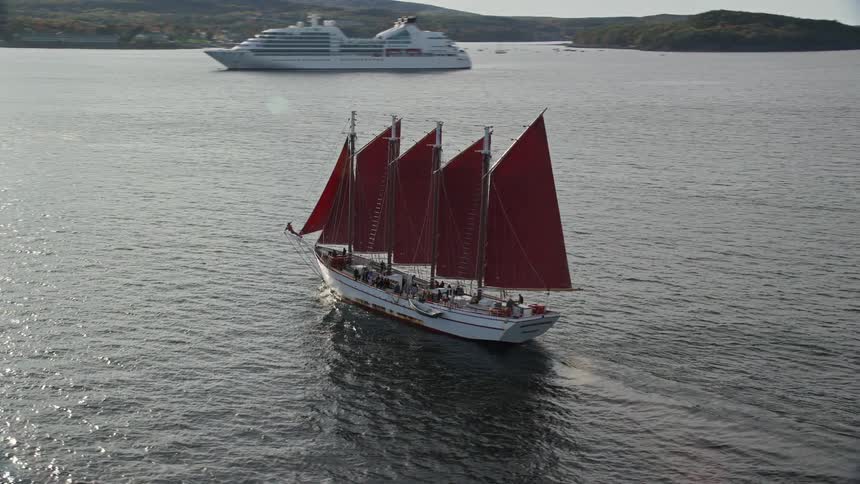 A sail boat and a cruise ship are traveling in the water