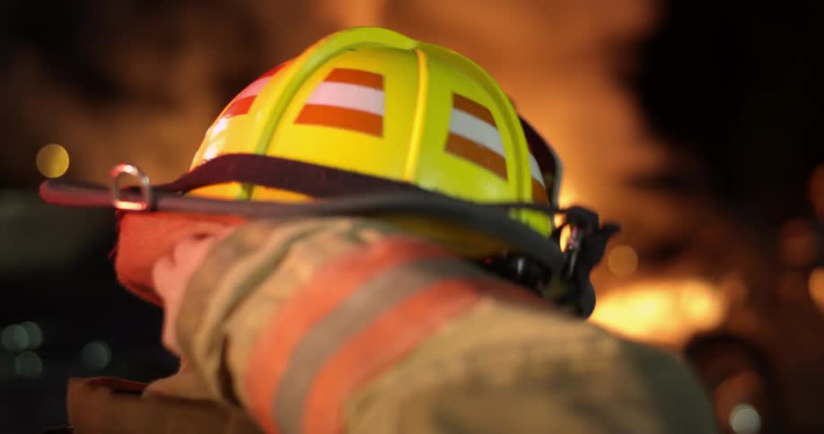 A firefighter putting his helmet on in front of a fire