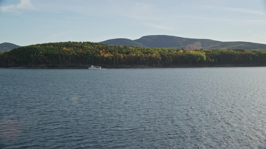 A boat riding just pass and beside an island covered with trees and vegetation