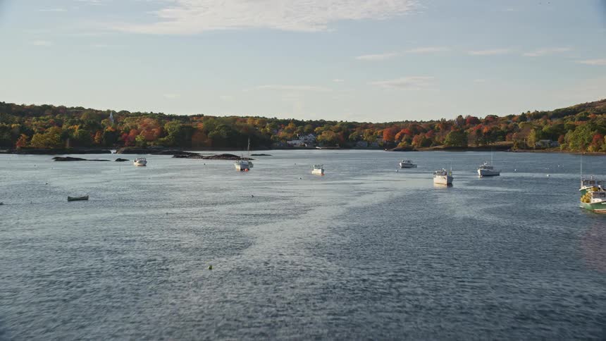 Aerial view of boats sailing down a river near an autumn forest