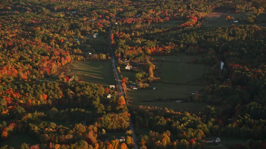 Aerial of highway through rural countryside surrounded by deciduous forest in the fall