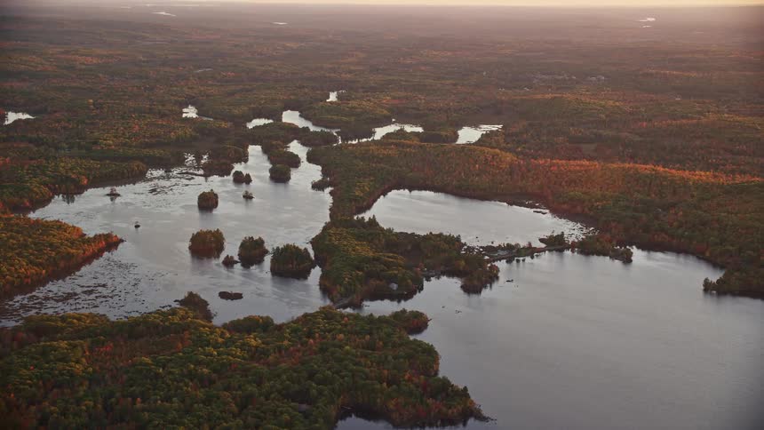 Aerial view of a lake and rivers surrounded by red and brown trees at sunset