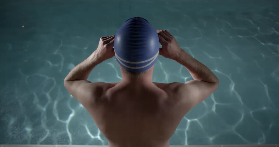 A swimmer putting goggles on and looking down at the water