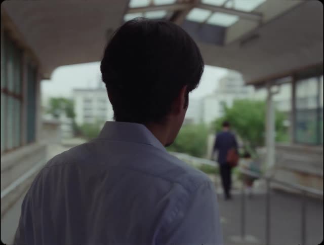 Man walks under shelter with windows and looks toward person walking away
