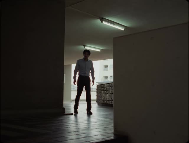A man walk into a building with dim light with florescent light shining from the ceiling
