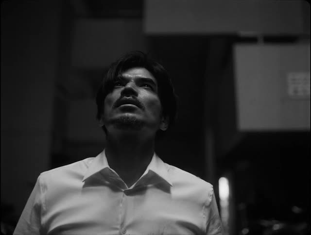 Black and white shot of a man walking on the city looking up