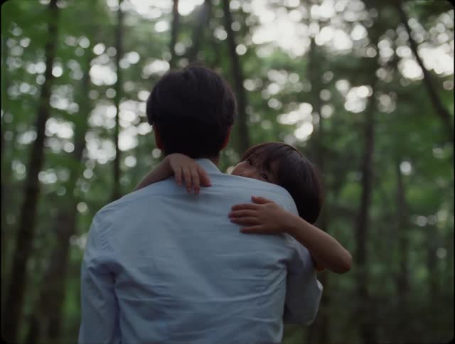 Man with a light blue shirt carries daughter in the woods