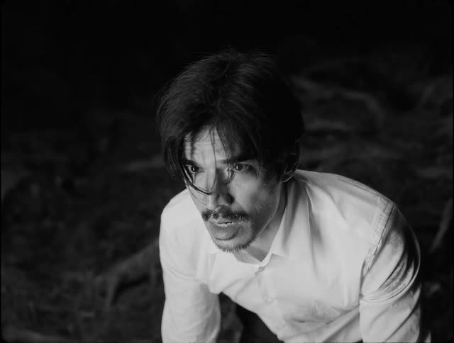 A terrified man with a mustache and wearing a white shirt looks upward