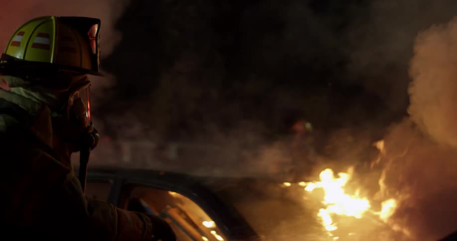 A fireman puts water on a burning car
