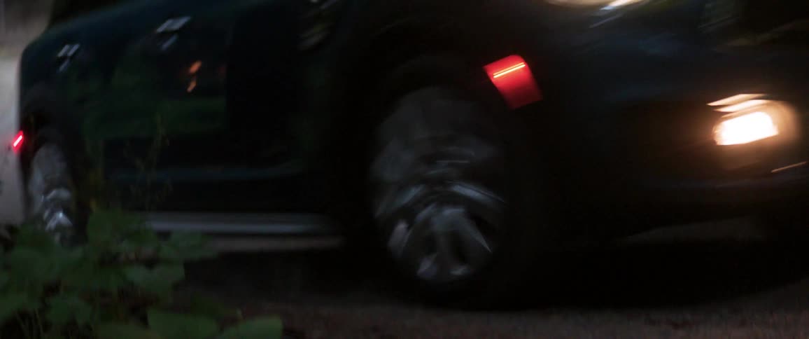 A black car moving with headlights on inside the forest at dusk