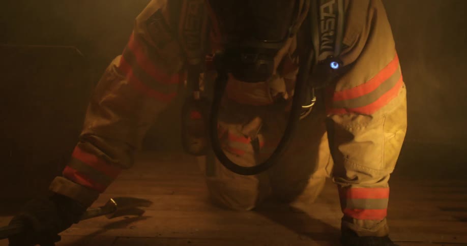Fireman crawls on floor holding a tool during a fire