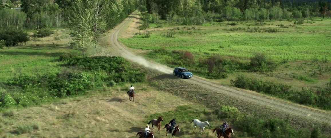 Blue suv driving on a small road amidst mountains with horses running