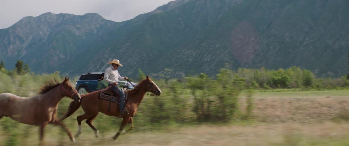 Men on cowboys hat riding horses and a car moving on a dusty road on a sunny day