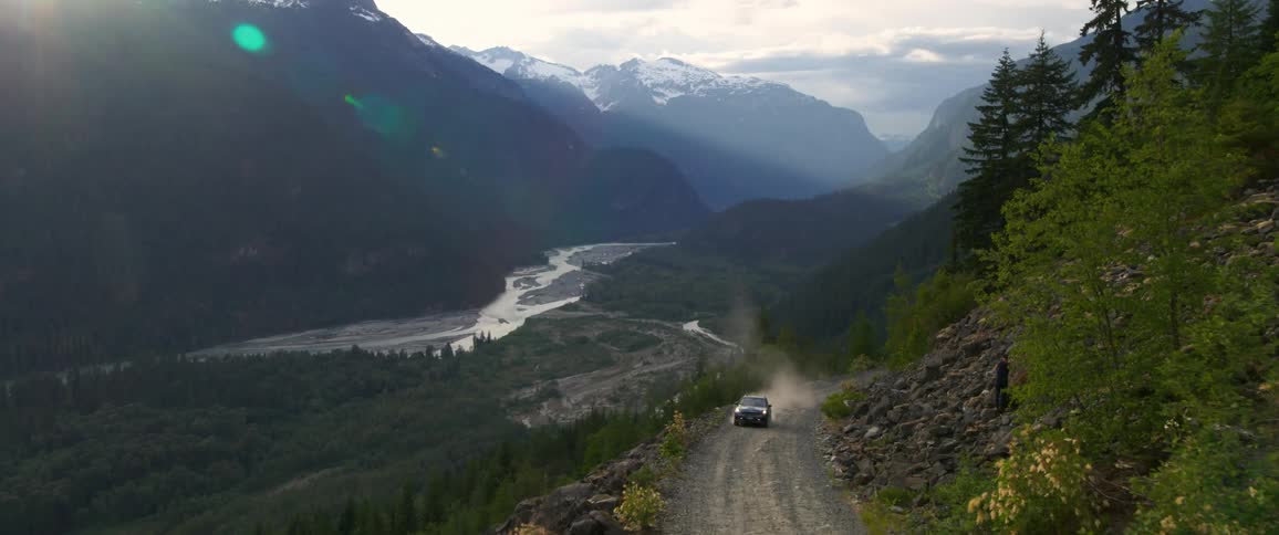 Car moving up on a dusty hill road at sunset