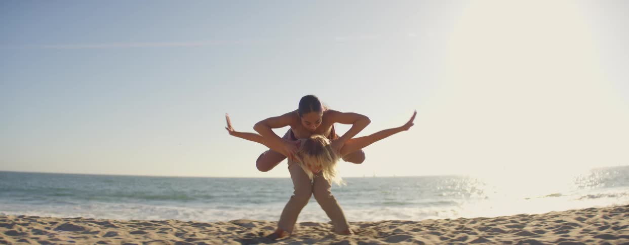 Two women dance on the beach near the sea with the bright sun shining