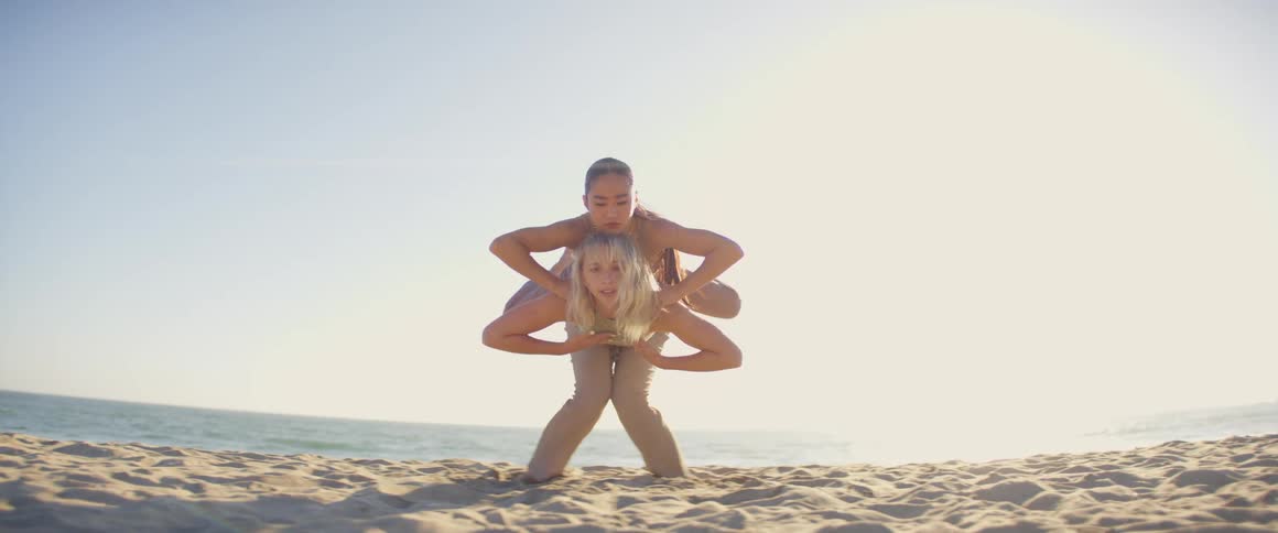 Two female dancers perform routine on sandy beach on sunny day