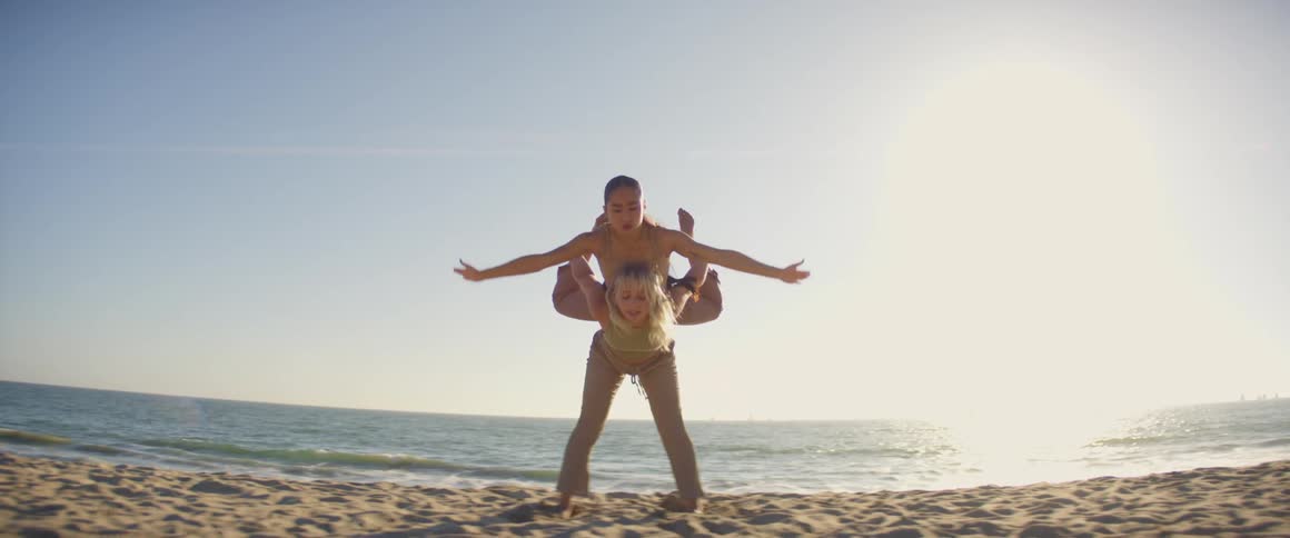 Two women dance on the beach near the sea with the bright sun shining