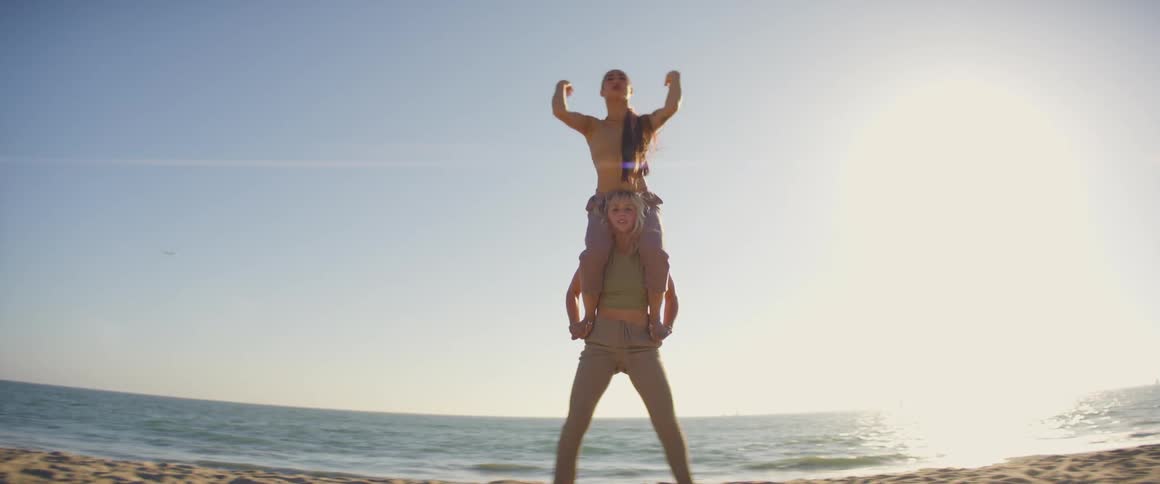 A woman is balancing a woman on her shoulders