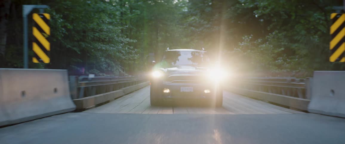 Vehicle with its headlights on crosses bridge over water in forest