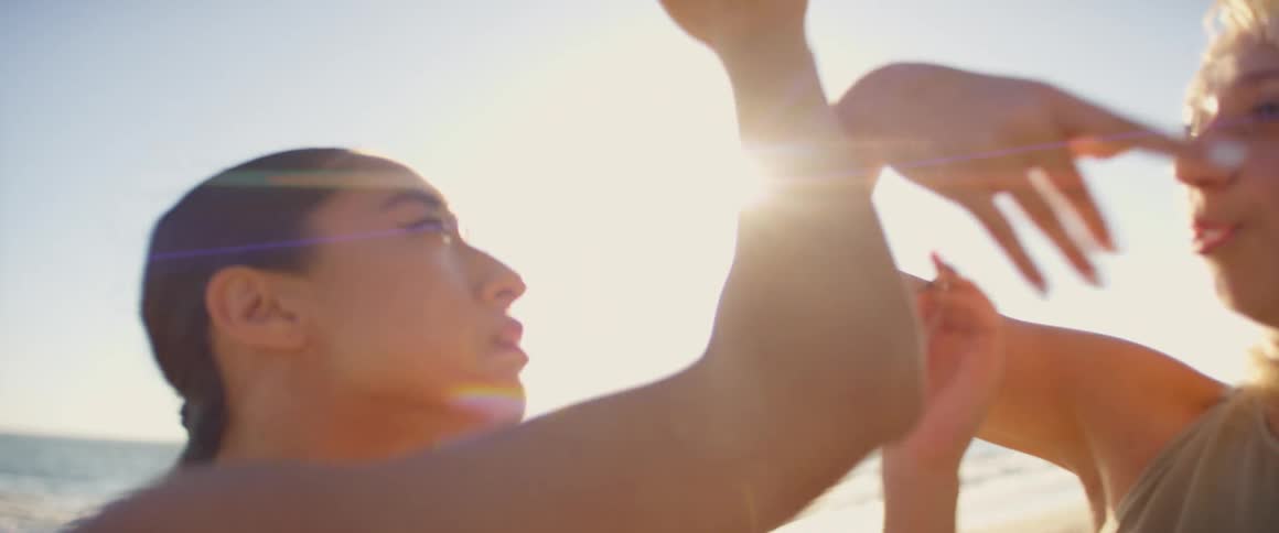 Two females doing slow dancing gestures with their hands at the beach on a sunny day