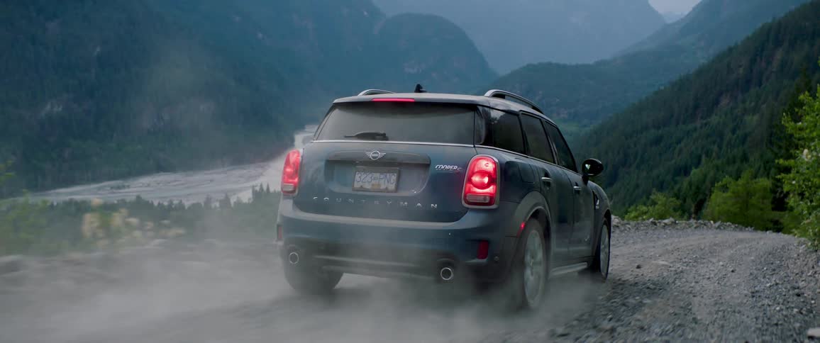 The car is driving on a gravel road by the river