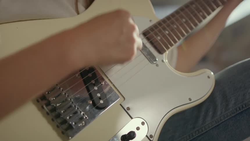 Person plays white guitar sitting indoors