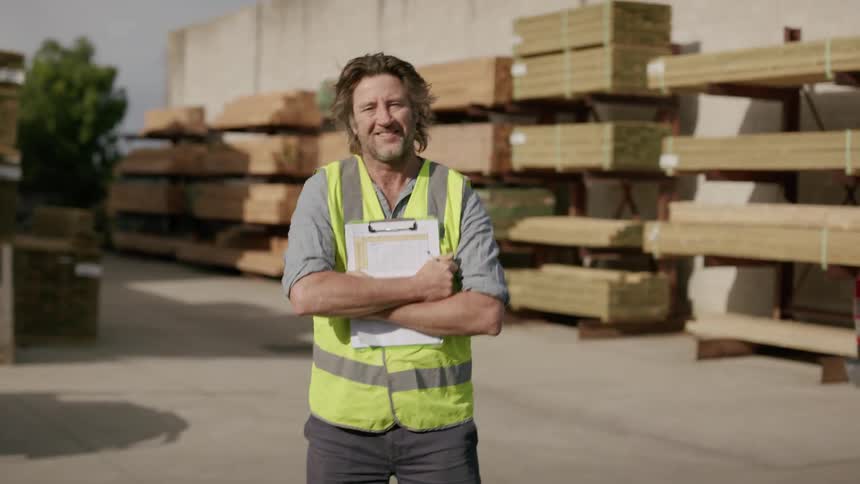 A man wearing a green vest smiles after writing on a notepad while standing at midday