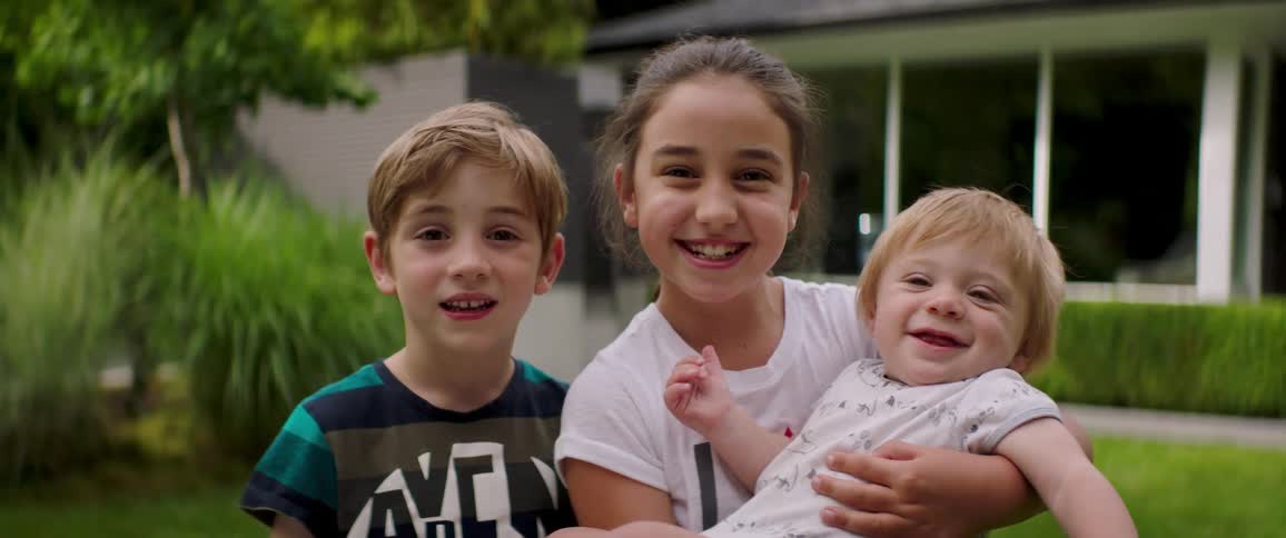 Siblings stand and smile while posing in front of house